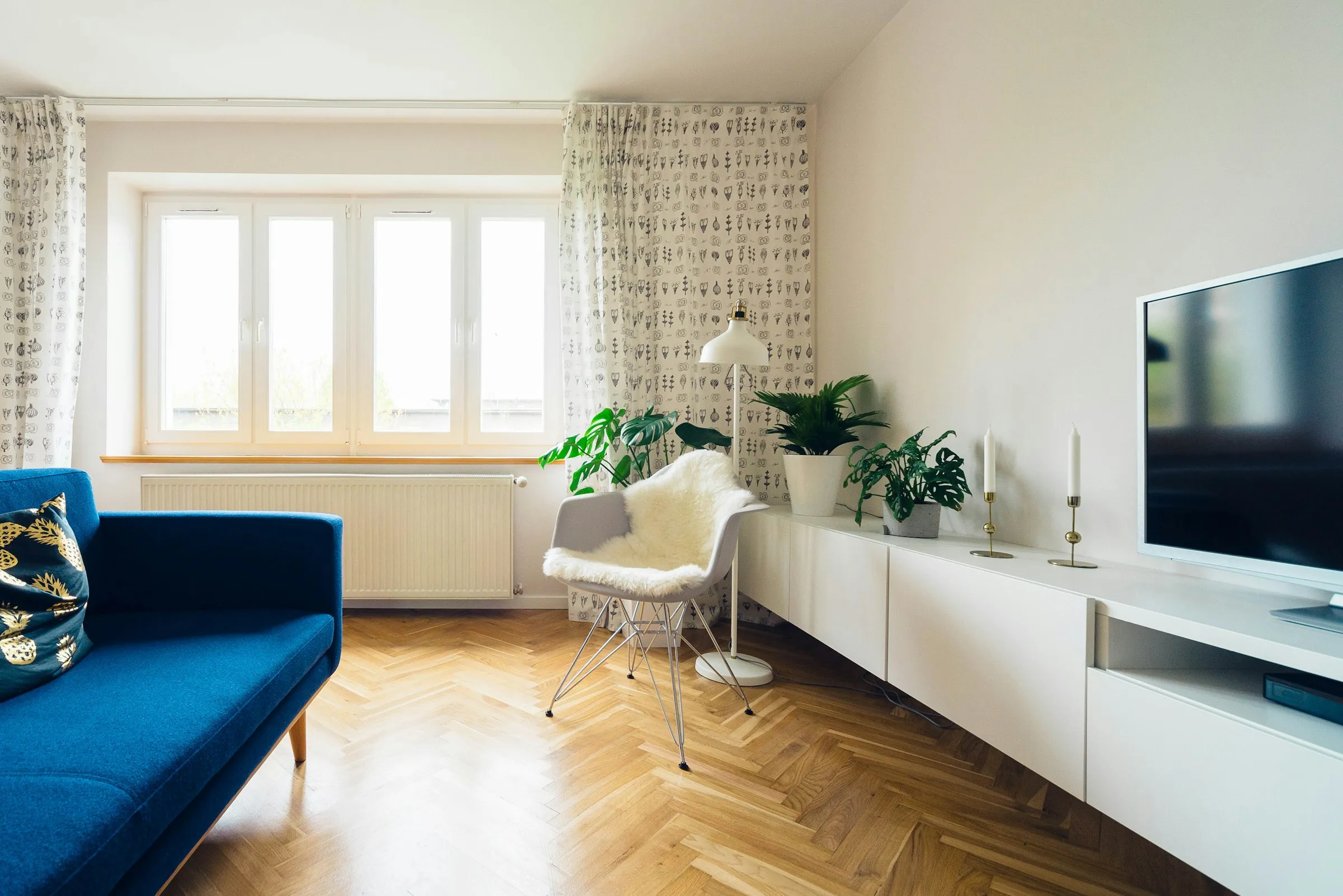Salon con suelo de espiga, sofa azul y plantas junto a la ventana