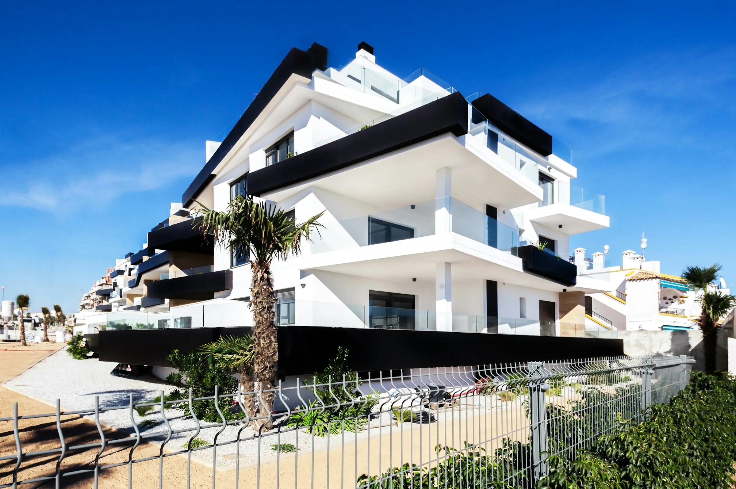 Edificio blanco de apartamentos con balcones y una palmera delante