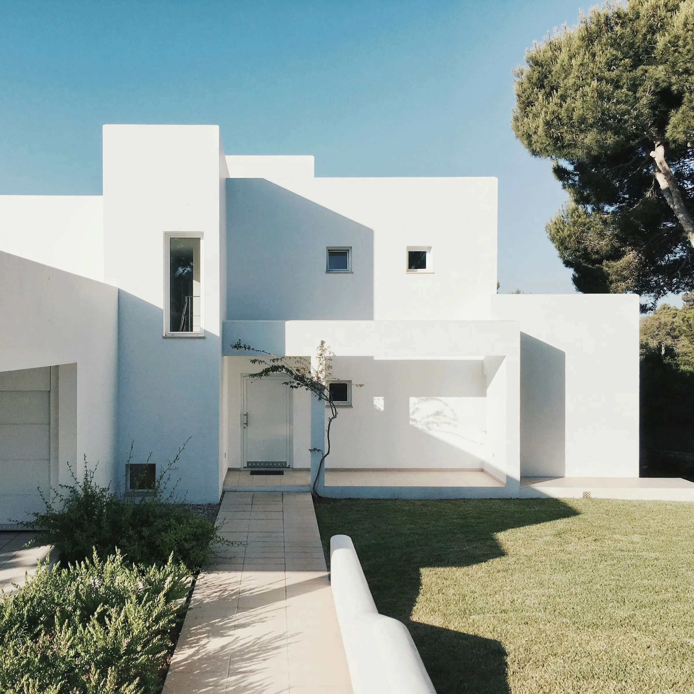Fachada blanca minimalista con huecos cuadrados y sombras marcadas