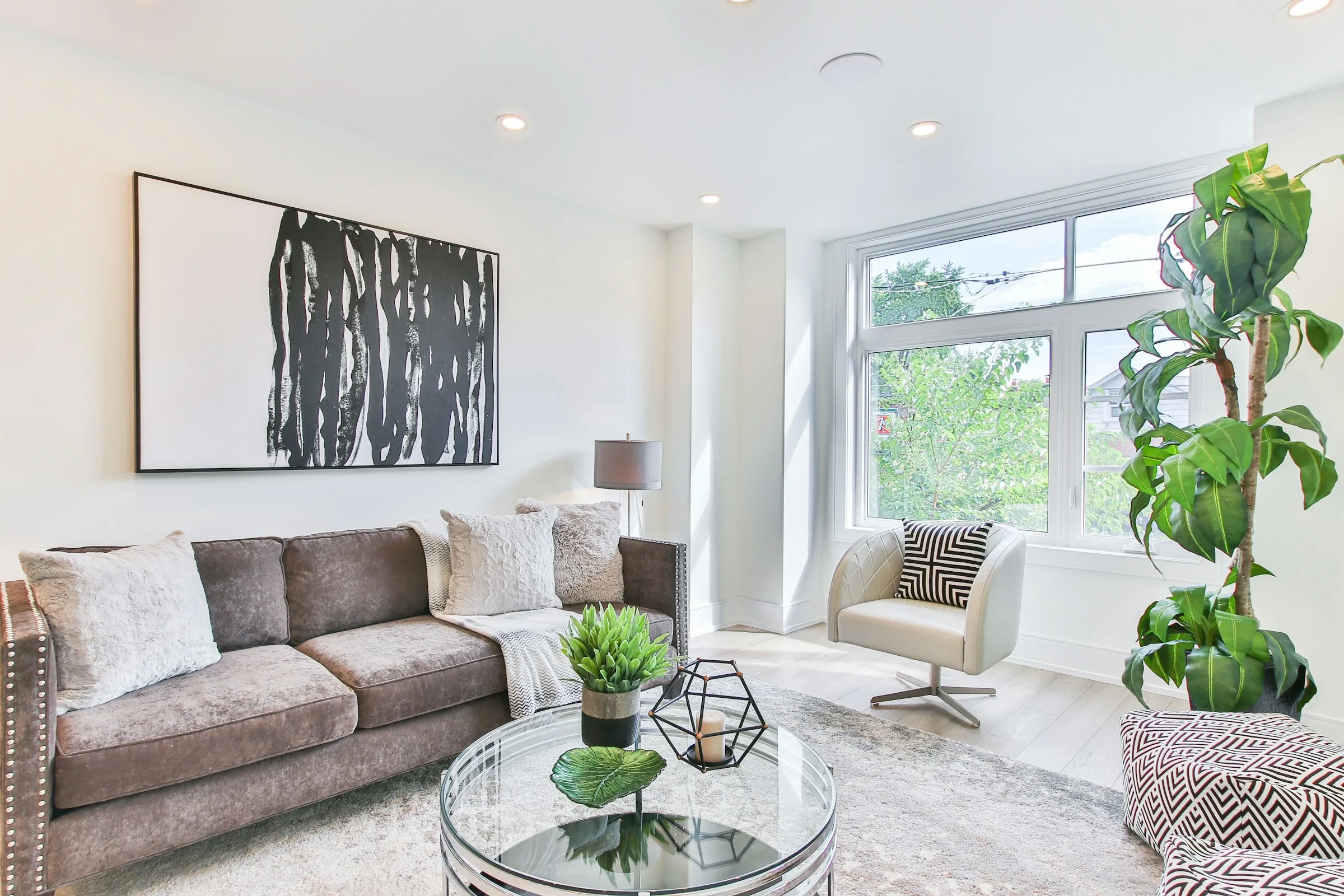 Salon claro con sofa gris, ventanales y plantas